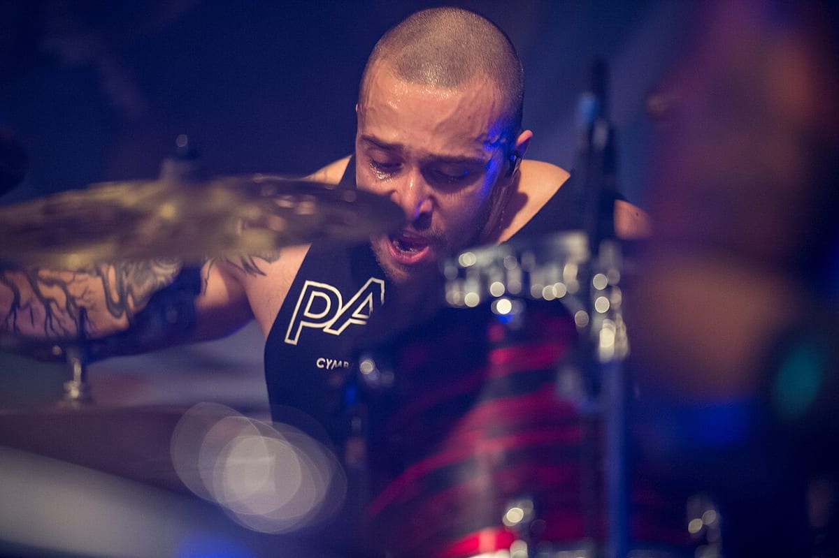 Eloy Casagrande mid-song in a Paiste vest, head shaved and arm tattooed, a cymbal blurred with the stroke