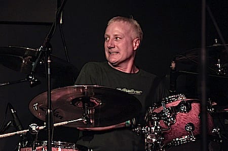 Gregg Bissonette behind a burl-finish kit, looking off to his left mid-set
