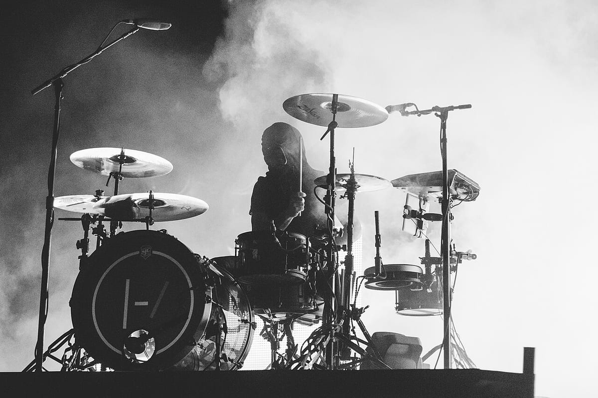 Josh Dun in silhouette behind his kit in black and white, smoke behind him and the twenty one pilots logo on the bass drum