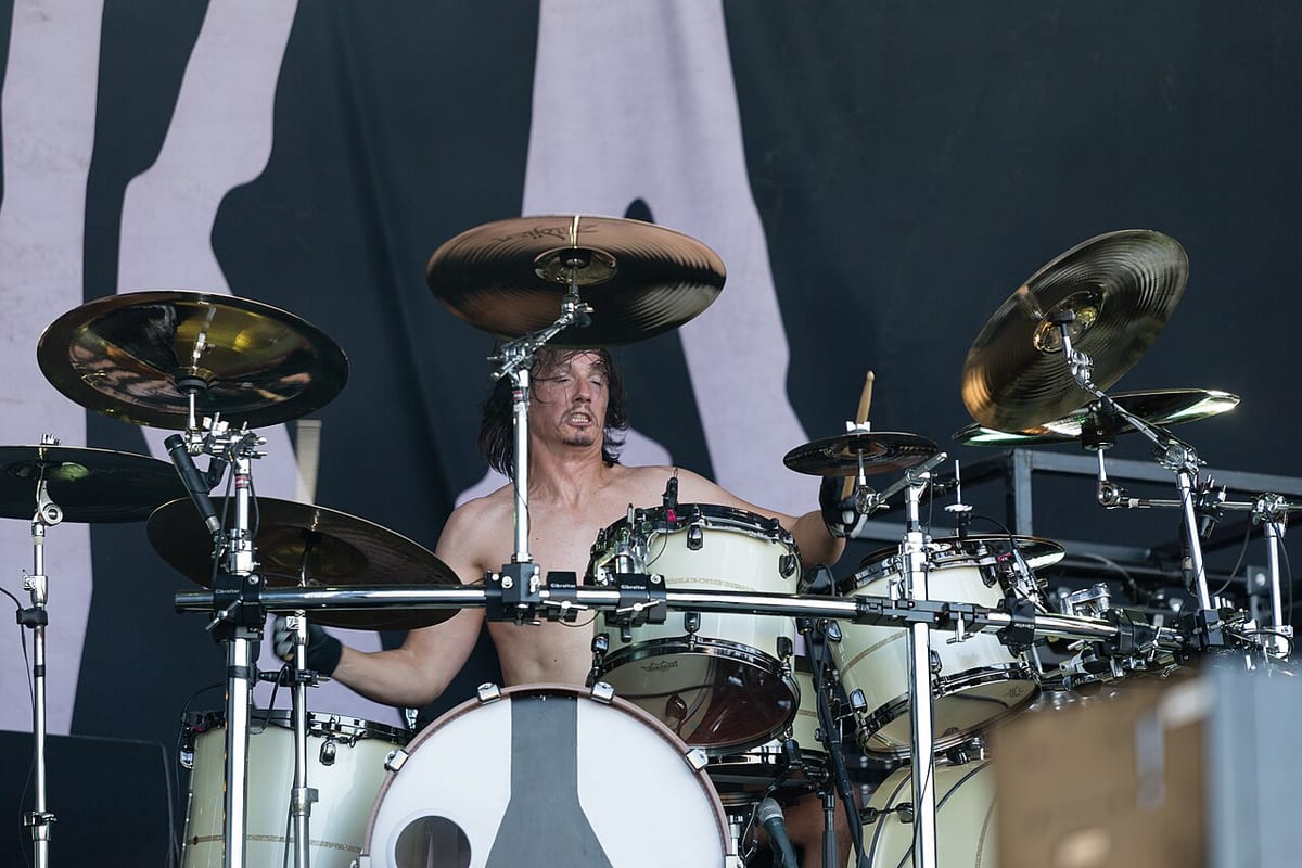 Mario Duplantier playing shirtless on a festival stage behind a cream kit ringed with cymbals