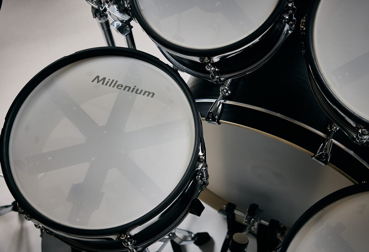 Close-up of the Millenium MPS-1500 Hybrid-X toms and bass drum, showing mesh heads over black wood shells with the internal trigger assembly visible through the mesh