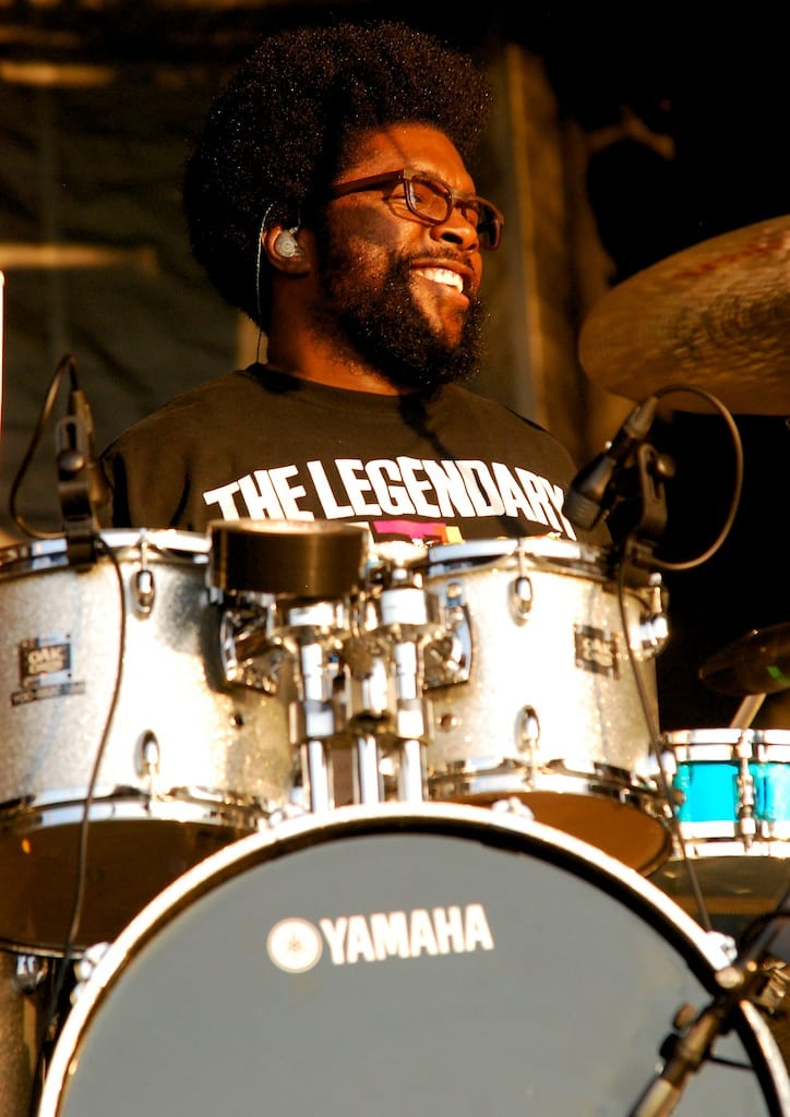 Questlove grinning behind a white sparkle Yamaha kit, in a T-shirt reading The Legendary