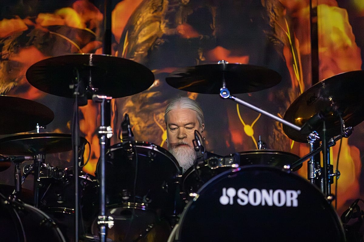 Tomas Haake behind a black Sonor kit, head down between the cymbals, lit by a fiery backdrop