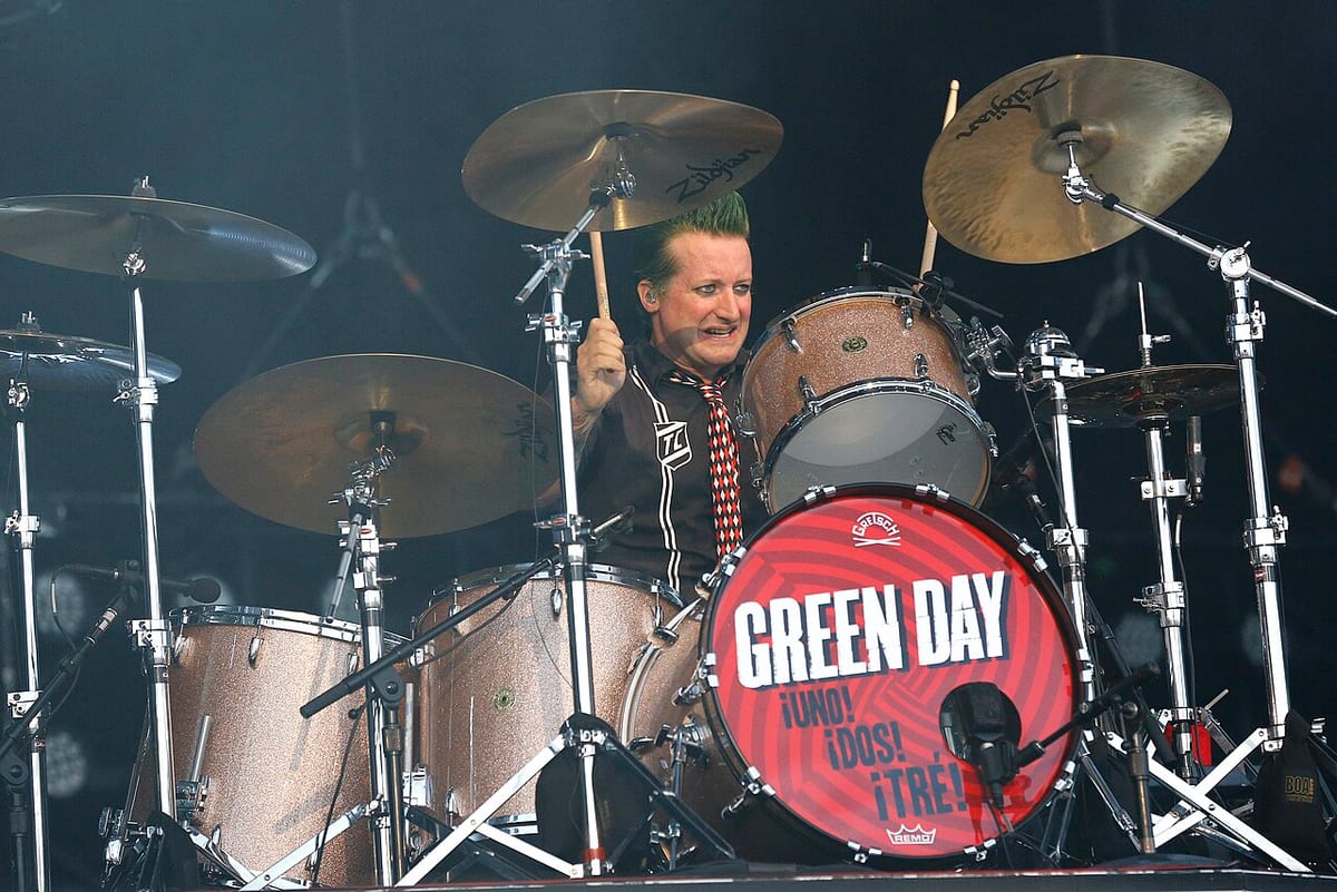 Tre Cool with green hair behind his Green Day kit, stick raised, bass drum head reading Uno Dos Tre