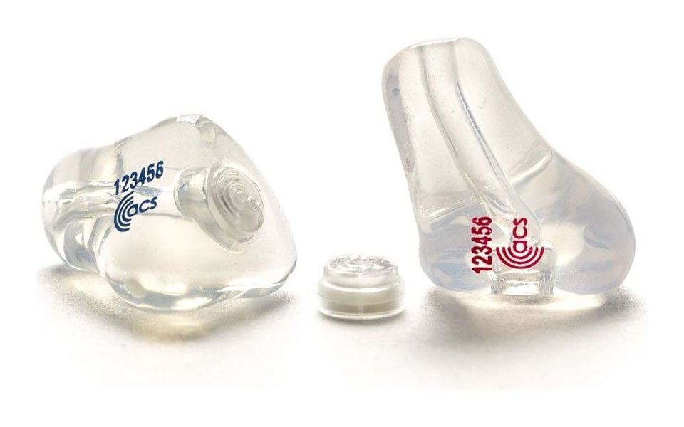 A pair of clear ACS custom-moulded earplugs with a small filter capsule between them