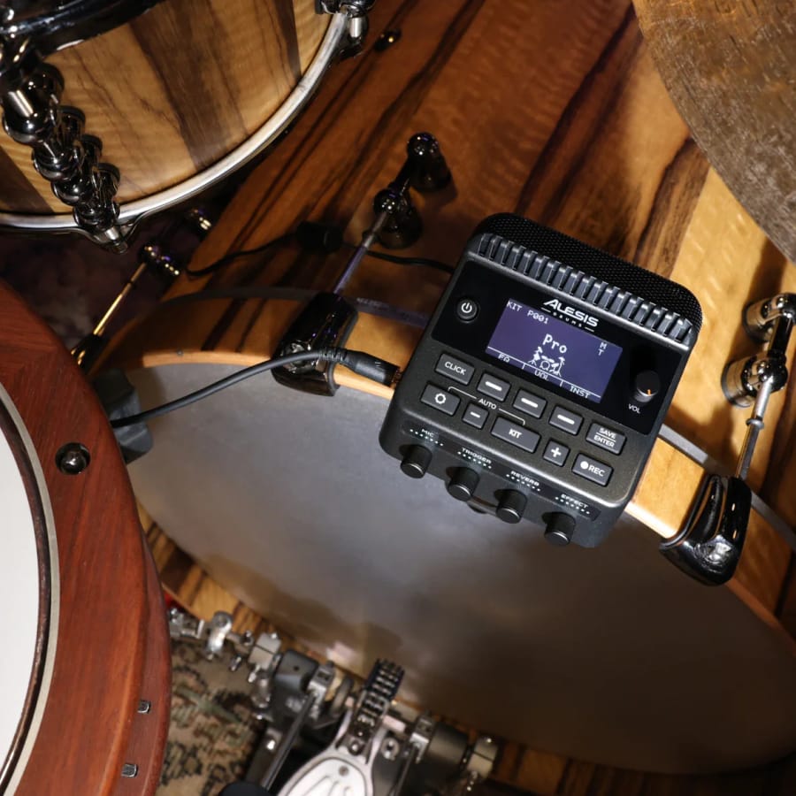 Overhead view of the Alesis KitStream mounted on a bass drum hoop, its screen showing kit P001 'Pro', with a small trigger clamped to the hoop beside it